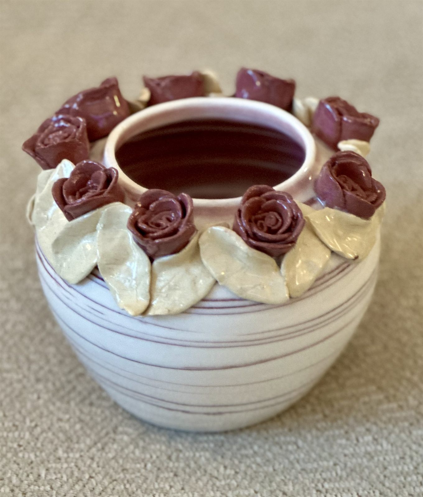 Deep mauve roses and pale sculpted leaves crowning a banded cream vessel